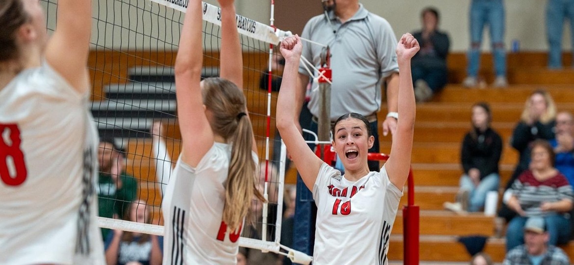 Volleyball players throw their hands up to celebrate scoring a point.